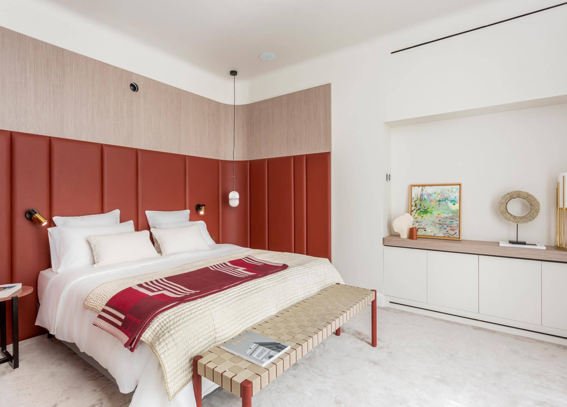 Camera da letto con boiserie imbottita rossa, rivestimento superiore in legno chiaro e mobile contenitore integrato.
