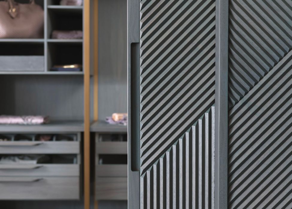 Detail of the handle of the sliding door clad in Relevo Tribeca 3D panelling by Foglie d&rsquo;Oro in a Sky Blue finish, featuring diagonal millwork, with a walk-in wardrobe in the background.
