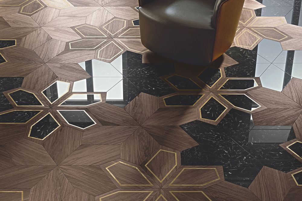 Напольное покрытие Azalea от Foglie d’Oro из древесины ореха со вставками из мрамора Nero Marquina и латуни, характеризующееся геометрическими цветочными мотивами; рядом с креслом из темной кожи.